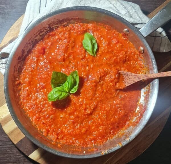 A pot of homemade marinara sauce simmering on a wooden cutting board.