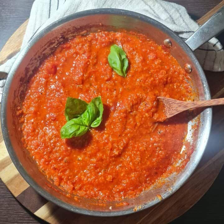 A pot of homemade marinara sauce simmering on a wooden cutting board.