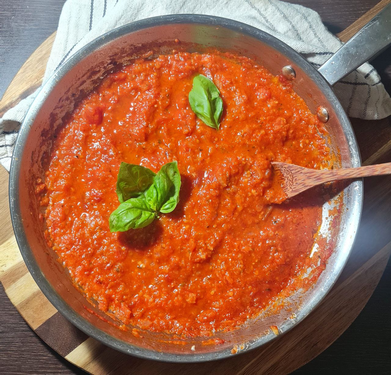 A pot of homemade marinara sauce simmering on a wooden cutting board.