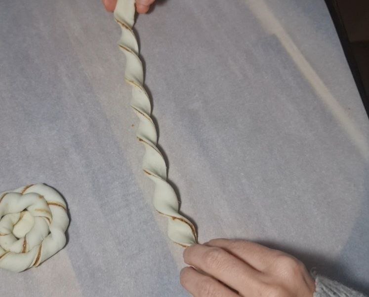 Hands twisting dough to create Biscoff swirls on a parchment-lined surface.