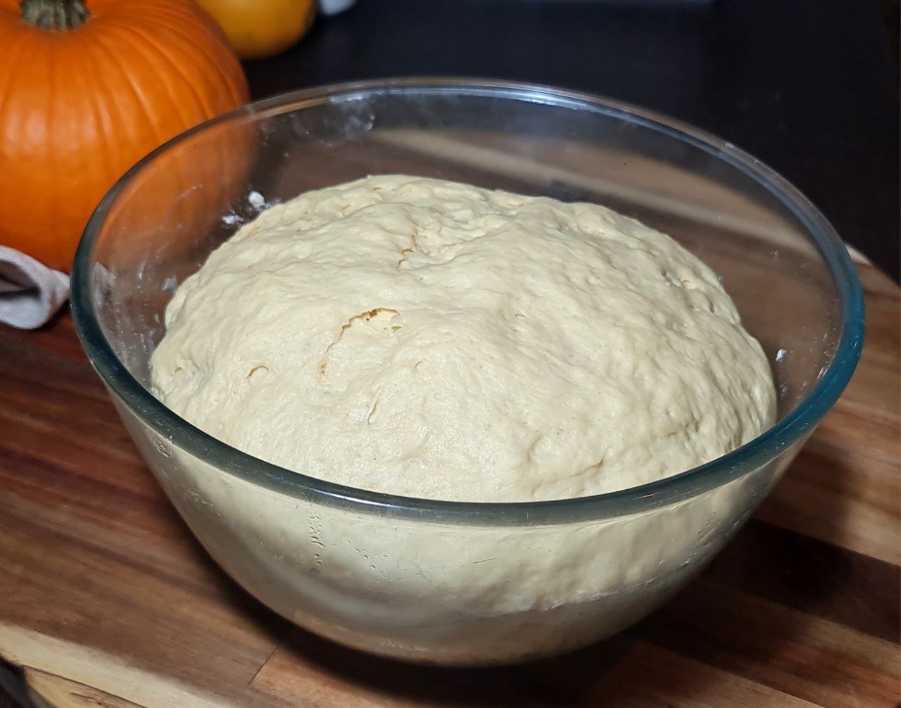  Bowl of risen pumpkin dinner roll dough ready for baking. Soft and airy dough for pumpkin dinner rolls after rising.