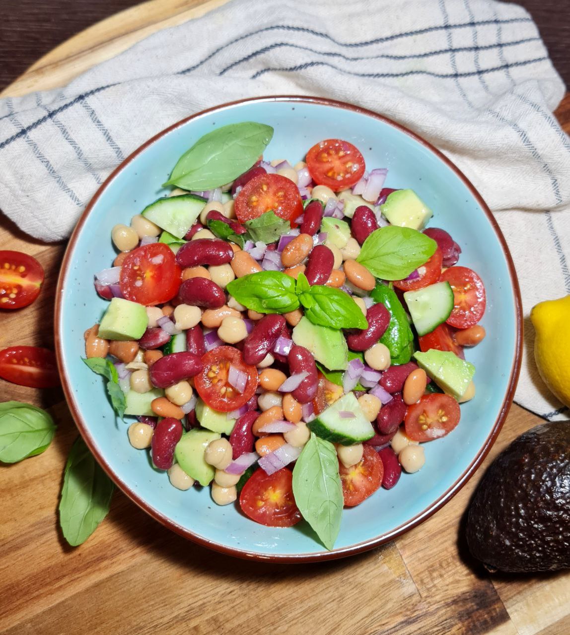 A plate of three bean salad with a wooden serving spoon and garnished with fresh herbs.