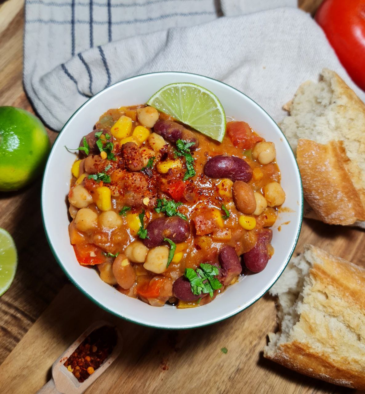 A bowl of vegan three bean chili served with a slice of lime and garnished with fresh cilantro.