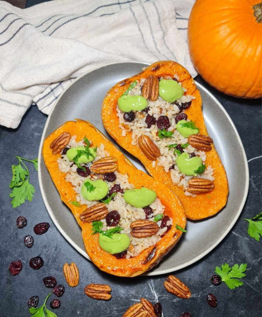 Stuffed butternut squash halves with rice, cranberries, pecans, and green sauce garnished with parsley on a gray plate. Savory stuffed butternut squash with rice, cranberries, pecans, and a vibrant green sauce.
