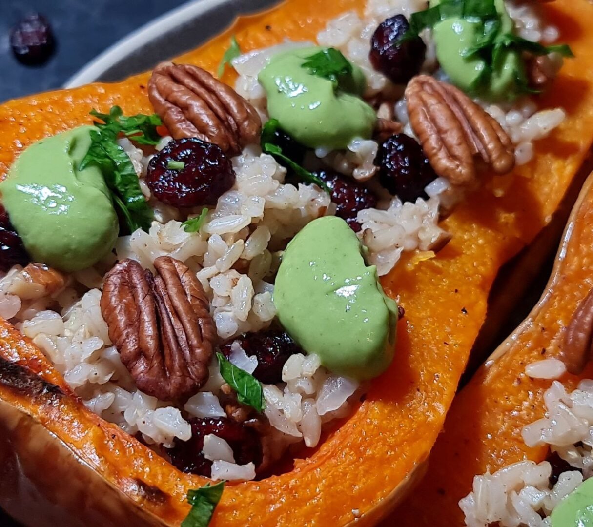 Close-up of stuffed butternut squash with rice, cranberries, pecans, green sauce, and parsley. A close-up view of the rich textures and vibrant colors in the stuffed butternut squash.