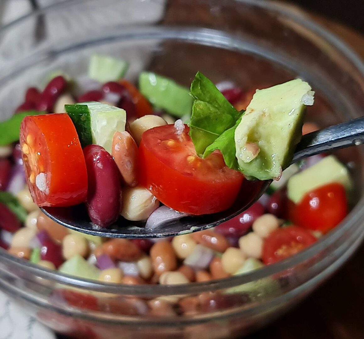 Close-up view of three bean salad with colorful beans, vegetables, and fresh herbs.