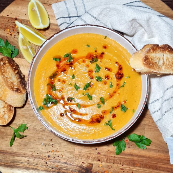 Bowl of creamy Turkish red lentil soup garnished with chopped herbs, served with crusty bread slices. Creamy Turkish red lentil soup garnished with fresh herbs and served with crusty bread.