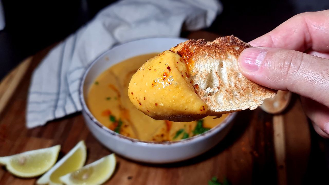  Close-up of a hand holding a piece of bread dipped in Turkish lentil soup. A delicious piece of bread dipped in creamy Turkish lentil soup.