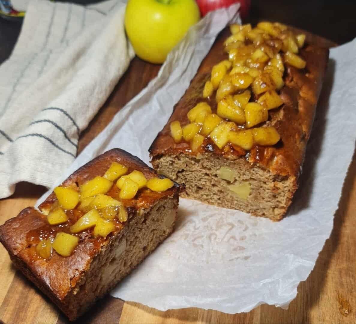 Moist vegan apple cake topped with caramelized apples, served on a rustic plate with a drizzle of syrup and a cinnamon stick garnish.