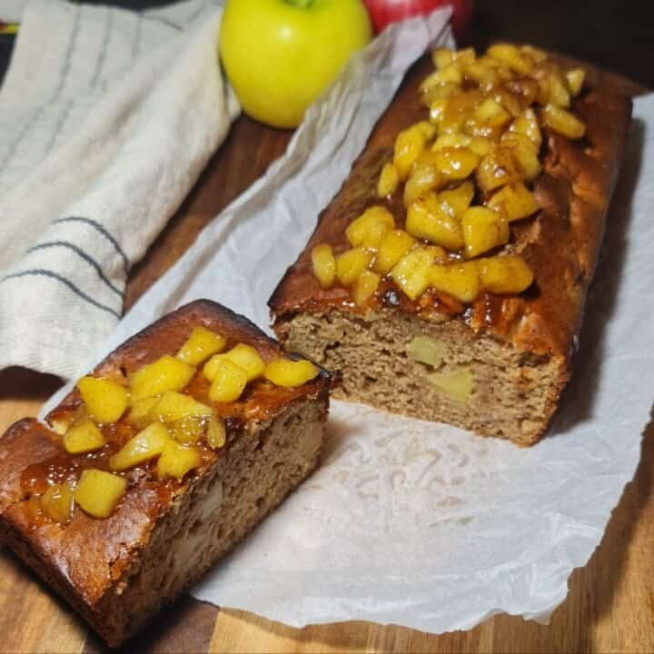 Moist vegan apple cake topped with caramelized apples, served on a rustic plate with a drizzle of syrup and a cinnamon stick garnish.