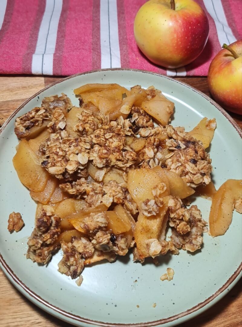 A plate of homemade vegan apple crisp with a crunchy oat topping, surrounded by fresh apples.  Delicious homemade vegan apple crisp served on a plate, perfect for a cozy dessert.