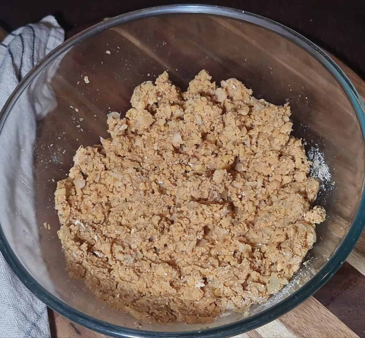 A glass bowl filled with a mixture of mashed chickpeas and other ingredients for making vegan chickpea meatballs.