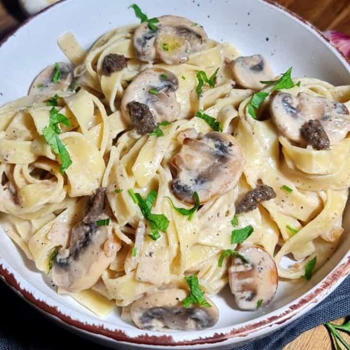 A bowl of vegan creamy mushroom and truffle pasta garnished with fresh herbs. Delicious vegan creamy mushroom and truffle pasta, perfect for a comforting meal.