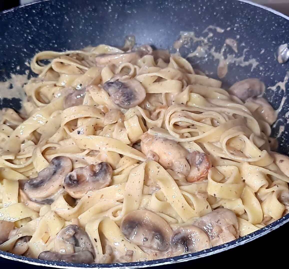 Vegan creamy mushroom and truffle pasta cooking in a pan, showing fettuccine noodles with creamy sauce and mushrooms. Vegan creamy mushroom and truffle pasta cooking to perfection.