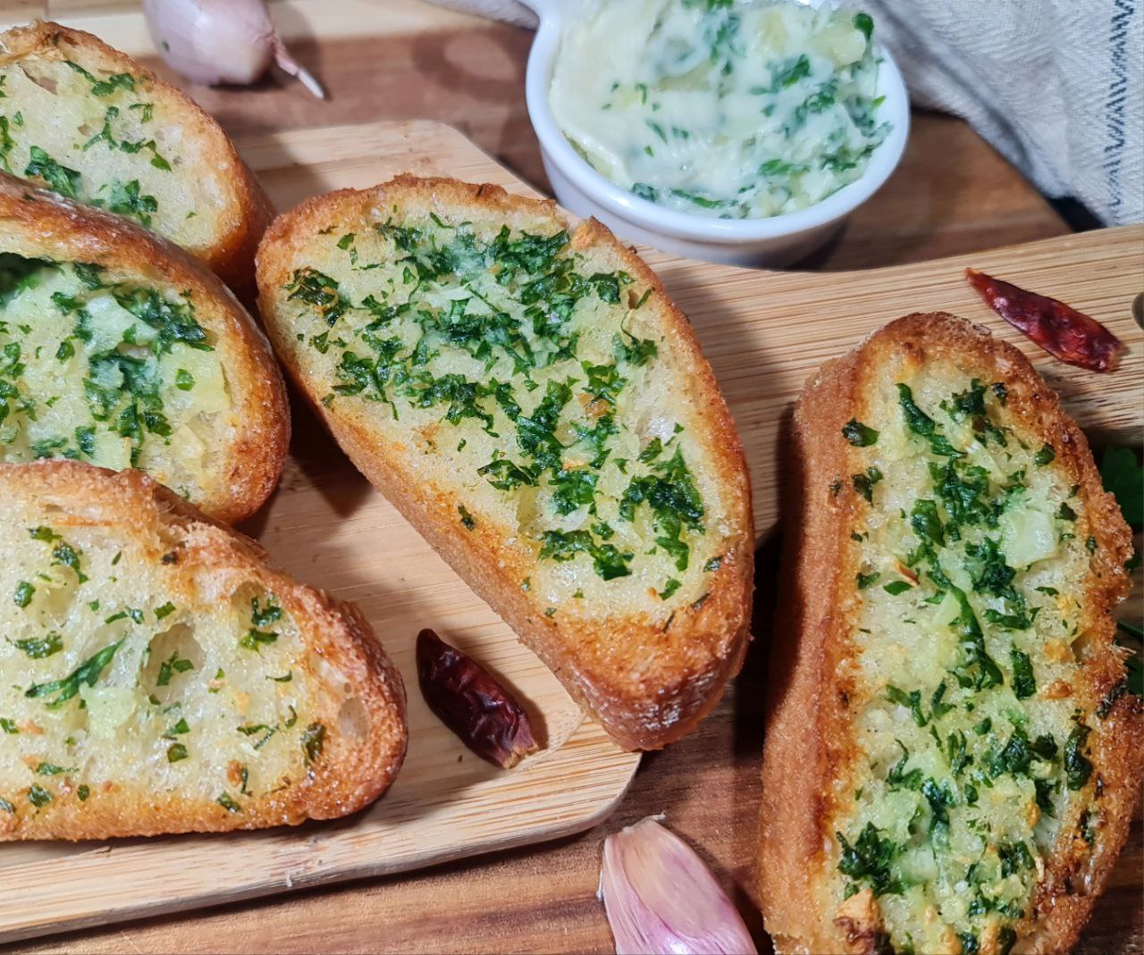 Slices of vegan garlic bread topped with fresh herbs on a wooden board, accompanied by a small bowl of herb-infused vegan butter. Delicious slices of vegan garlic bread with fresh herbs, perfect for any meal.