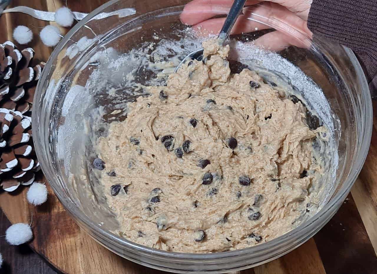 A glass bowl filled with vegan gingerbread chocolate chip cookie dough being mixed with a spoon.