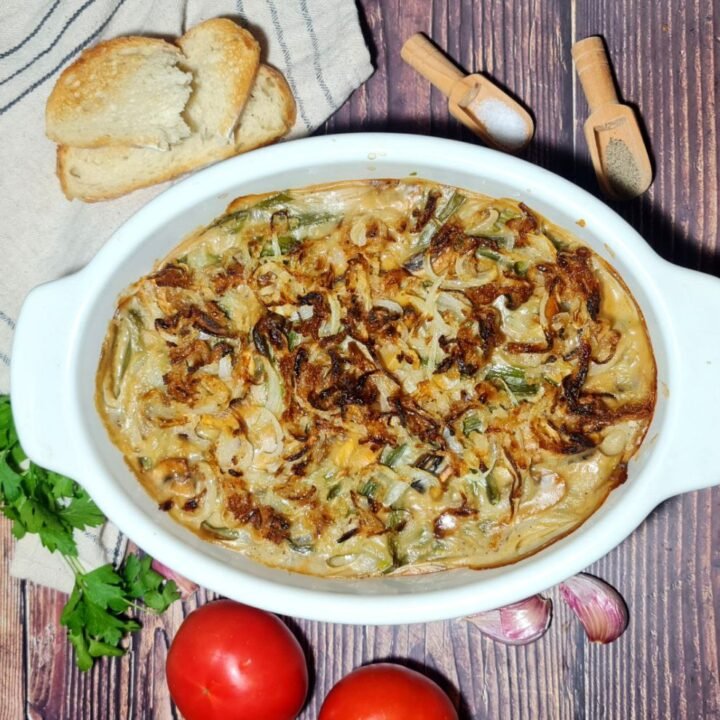 Freshly baked vegan green bean casserole in a white baking dish. Creamy, flavorful vegan green bean casserole topped with crispy onions, perfect for holiday dinners.