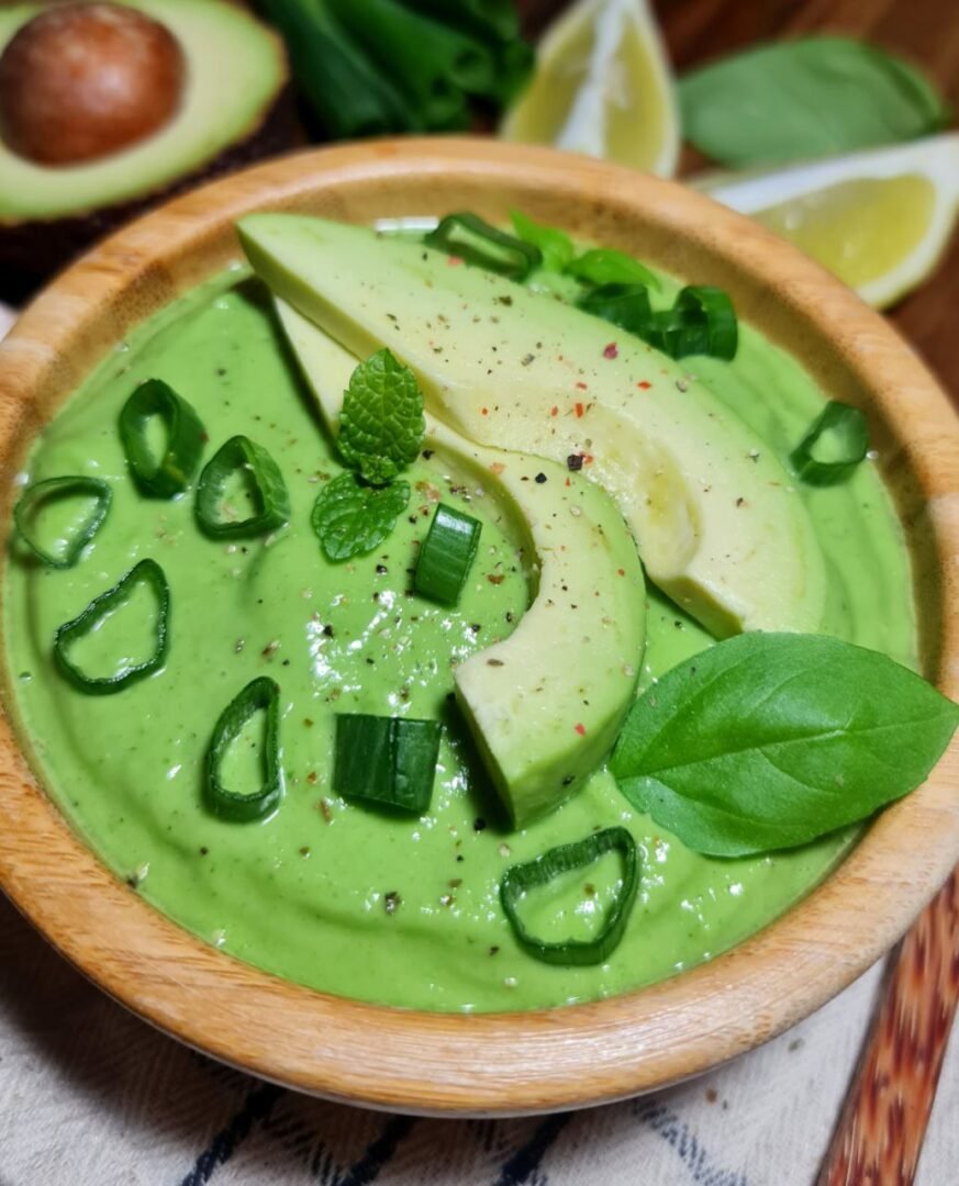 a bowl of green soup with avocado slices and herbs