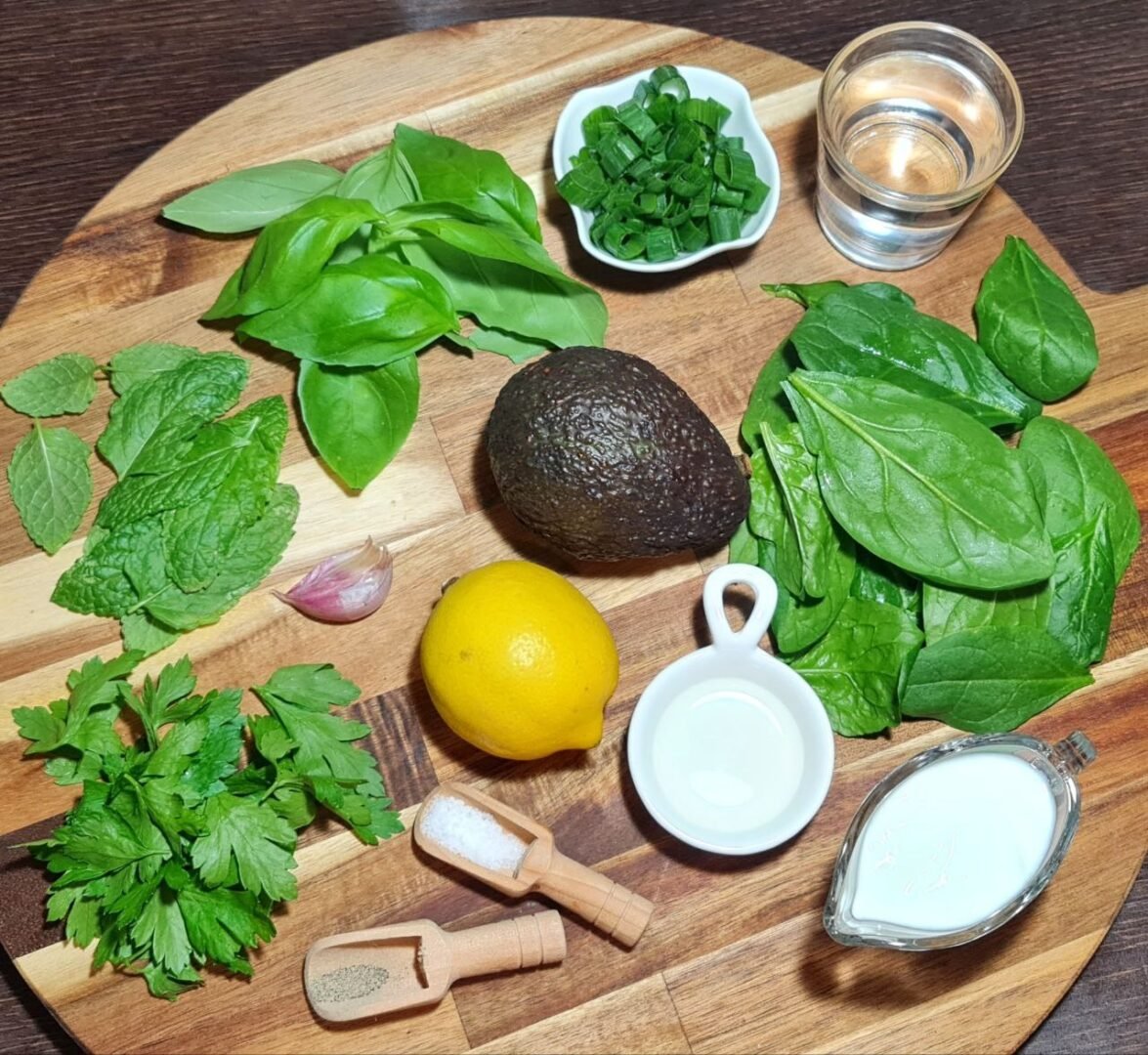 Fresh ingredients for vegan green goddess dressing on a wooden board. Fresh herbs and vegetables ready for a homemade vegan green goddess dressing.
