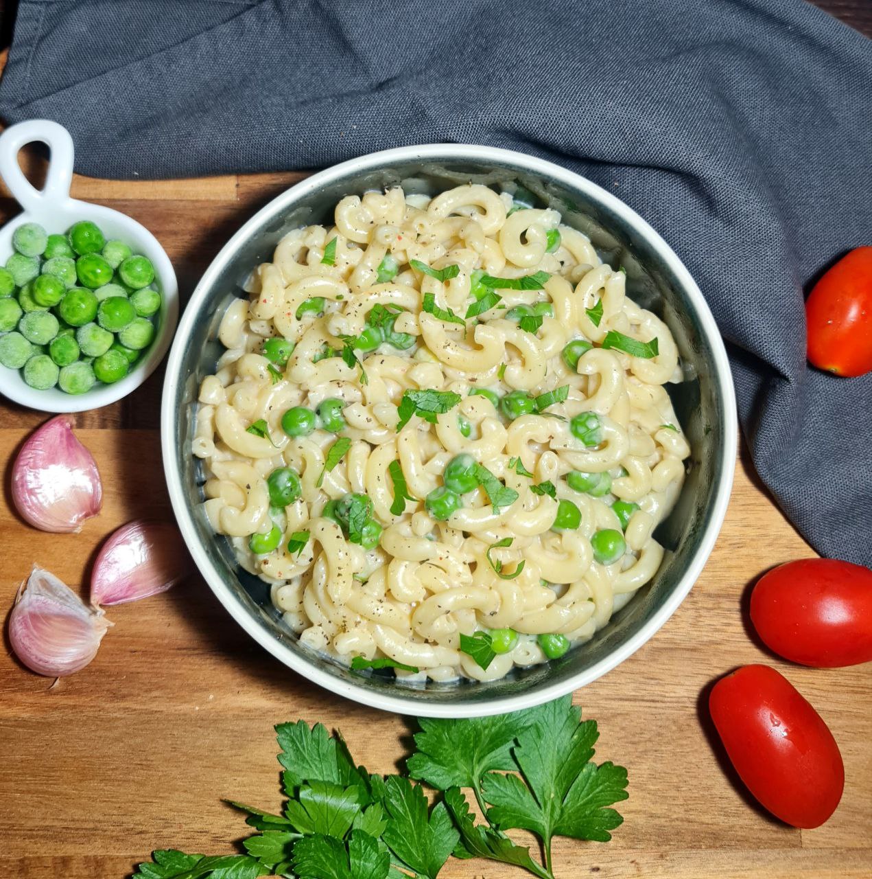 Creamy vegan macaroni and peas garnished with fresh parsley in a bowl on a wooden surface. A hearty bowl of Vegan Mac and Peas, perfect for a quick and comforting meal.