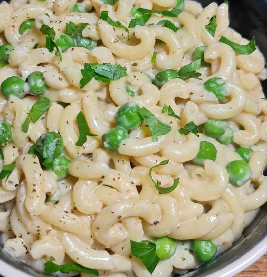 Detailed view of creamy vegan macaroni and peas garnished with fresh parsley and black pepper.