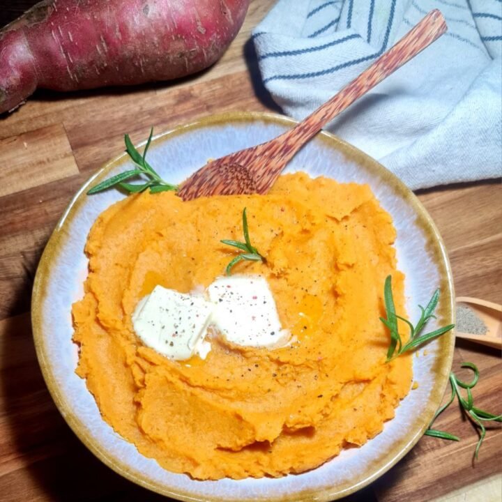 Bowl of creamy vegan mashed sweet potatoes with melting vegan butter and rosemary garnish. Creamy vegan mashed sweet potatoes topped with vegan butter and fresh rosemary.