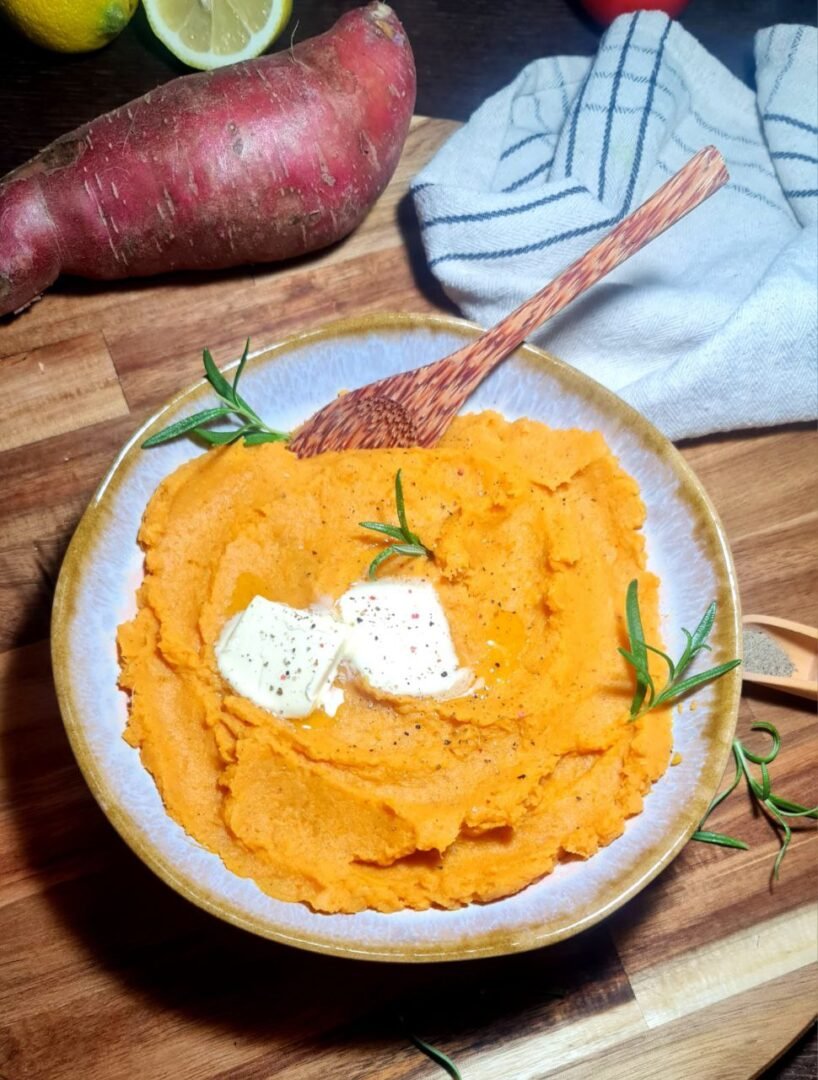 Bowl of creamy vegan mashed sweet potatoes with melting vegan butter and rosemary garnish. Creamy vegan mashed sweet potatoes topped with vegan butter and fresh rosemary.