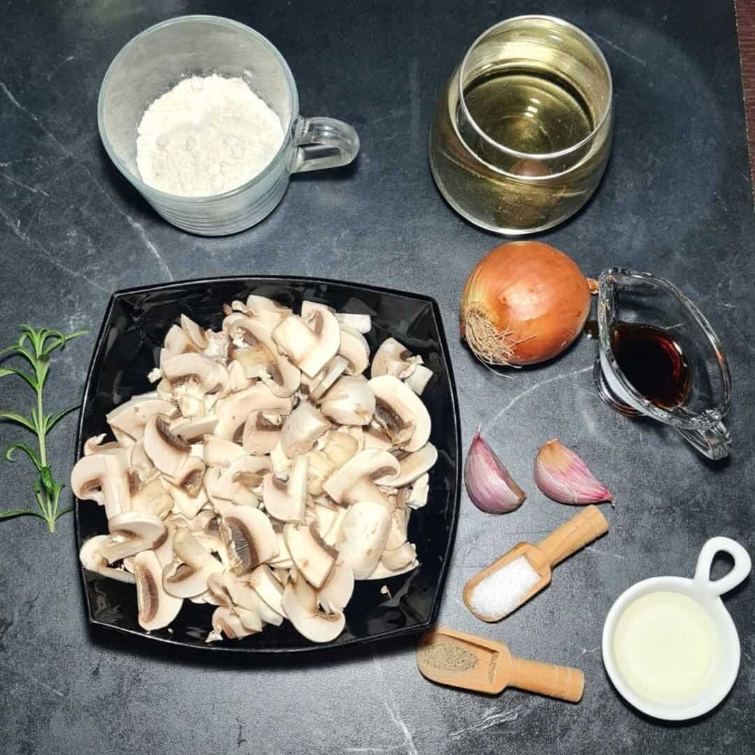  Ingredients for vegan mushroom gravy including chopped mushrooms, flour, white wine, onion, garlic, soy sauce, salt, pepper, oil, and rosemary. 