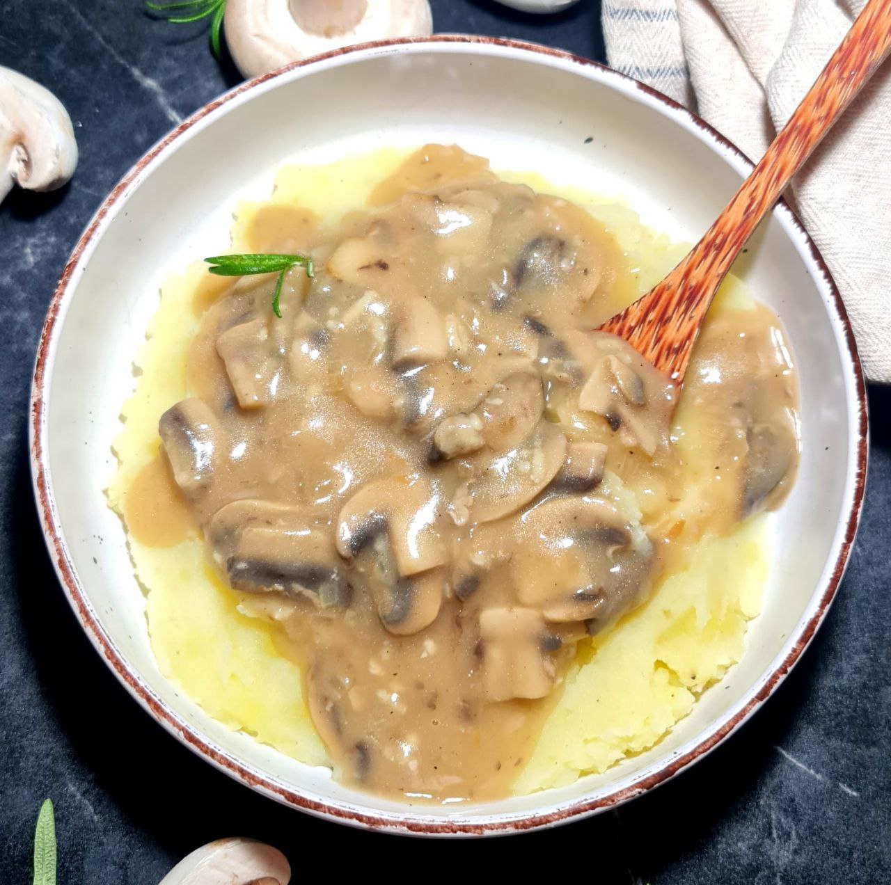 A bowl of vegan mushroom gravy served over mashed potatoes with a wooden spoon. Vegan mushroom gravy served over creamy mashed potatoes.