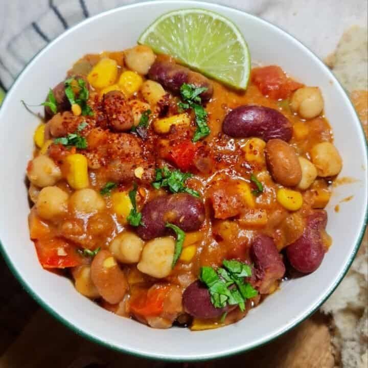 A bowl of vegan three bean chili topped with avocado slices, sour cream, and tortilla chips.