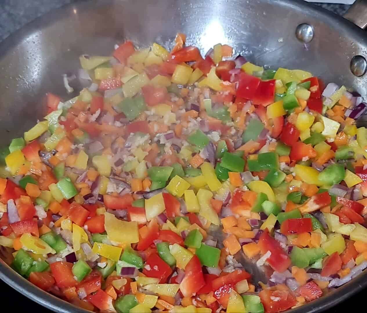 A pot of vegan three bean chili simmering on the stove with a wooden spoon for stirring.