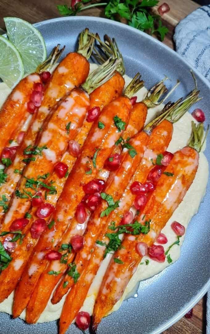 a plate of rosted carrots with hummus, pomegranate seeds, chopped parsley and tahini sauce.