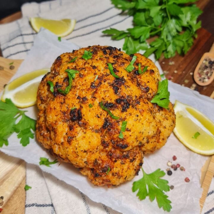 Whole roasted cauliflower garnished with fresh herbs and lemon wedges. A beautifully seasoned whole roasted cauliflower garnished with fresh herbs and served with lemon wedges.