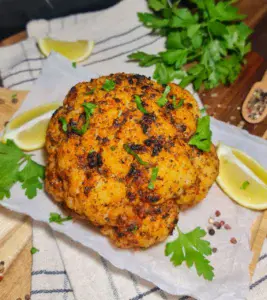Whole roasted cauliflower garnished with fresh herbs and lemon wedges. A beautifully seasoned whole roasted cauliflower garnished with fresh herbs and served with lemon wedges.