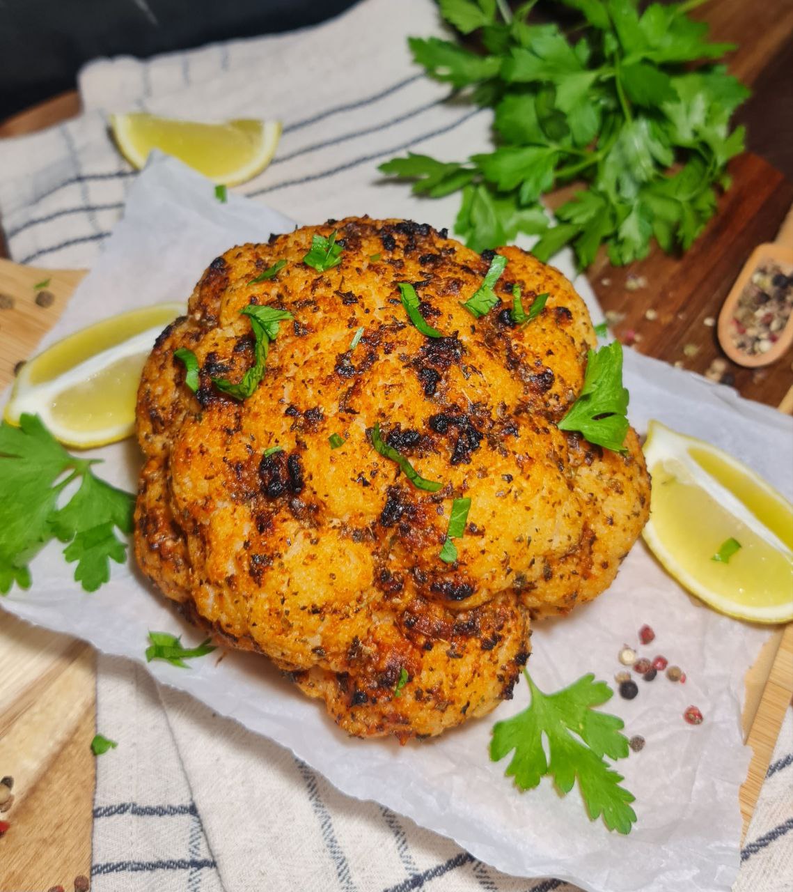 Whole roasted cauliflower garnished with fresh herbs and lemon wedges. A beautifully seasoned whole roasted cauliflower garnished with fresh herbs and served with lemon wedges.