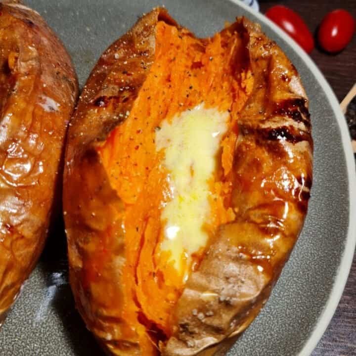 A close-up of a baked sweet potato split open with melted butter and seasoning on a gray plate.