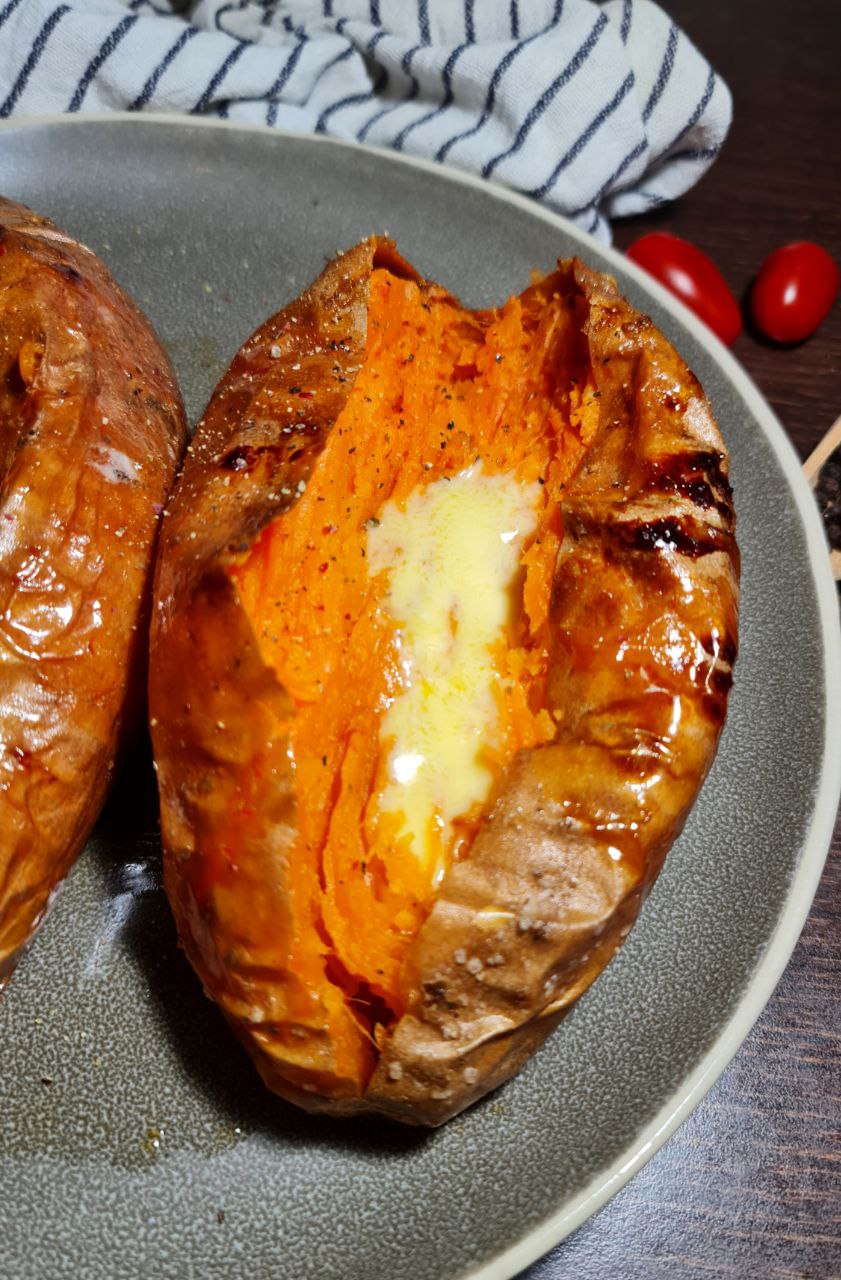 A close-up of a baked sweet potato split open with melted butter and seasoning on a gray plate.