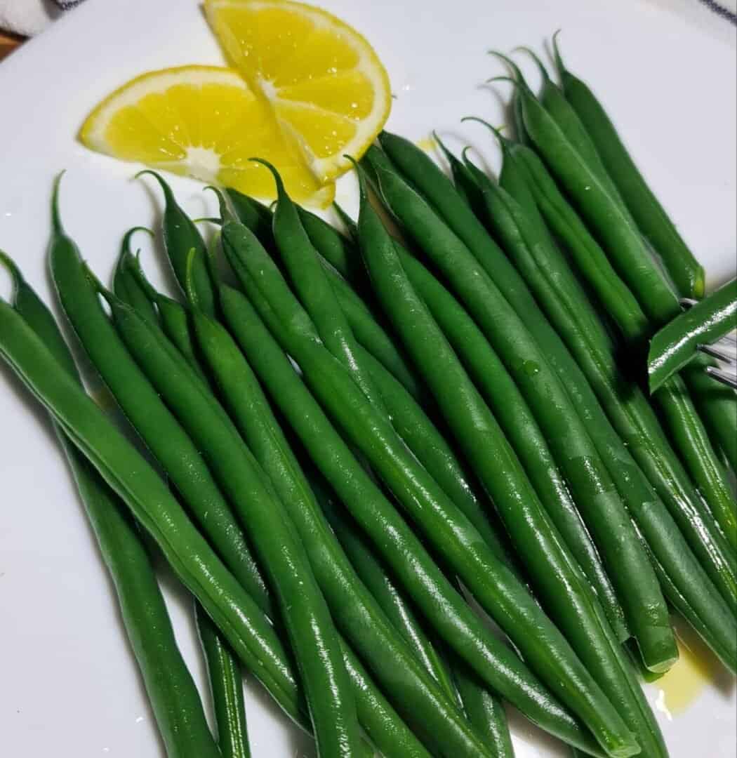  Freshly boiled green beans served with lemon slices on a white plate.