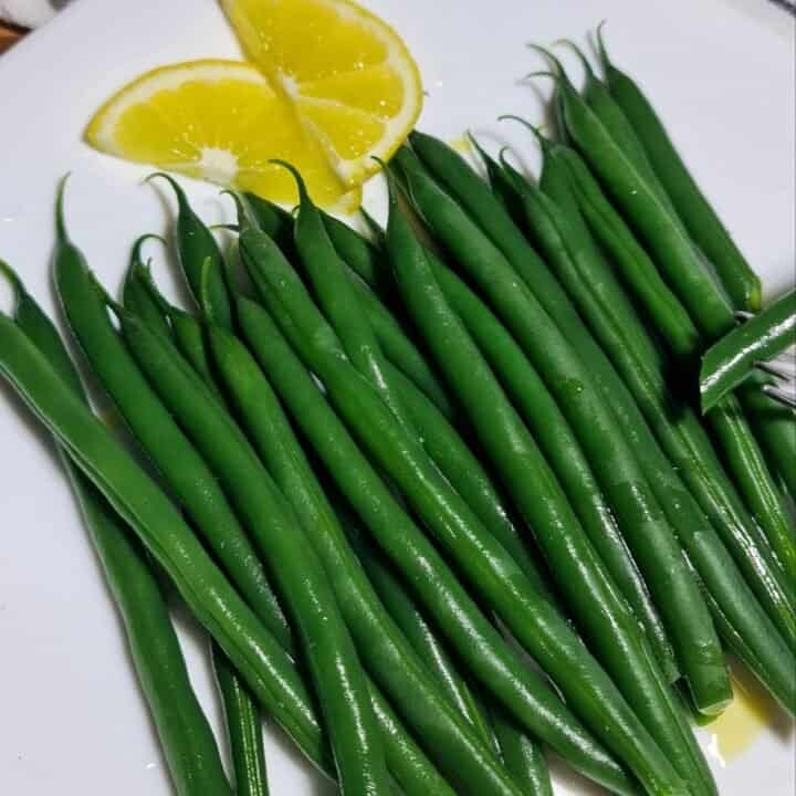 Freshly boiled green beans served with lemon slices on a white plate.