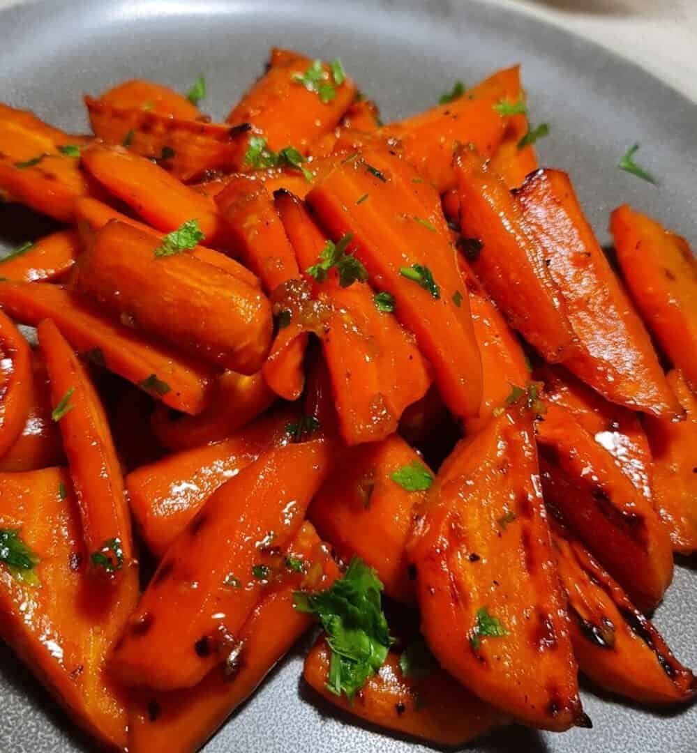 Glazed brown sugar carrots garnished with fresh herbs on a gray plate.