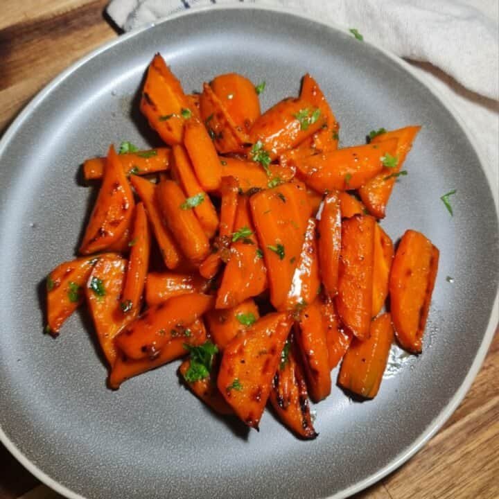 A plate of glazed brown sugar carrots garnished with fresh herbs.