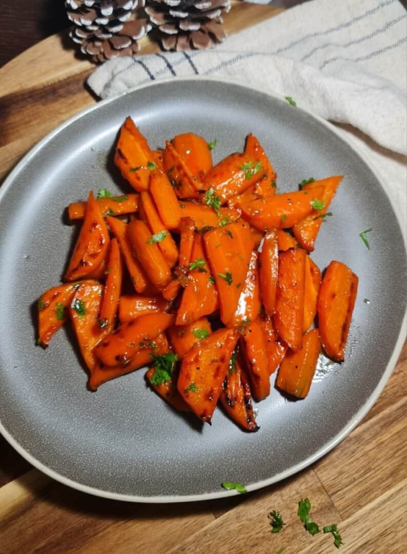 A plate of glazed brown sugar carrots garnished with fresh herbs.