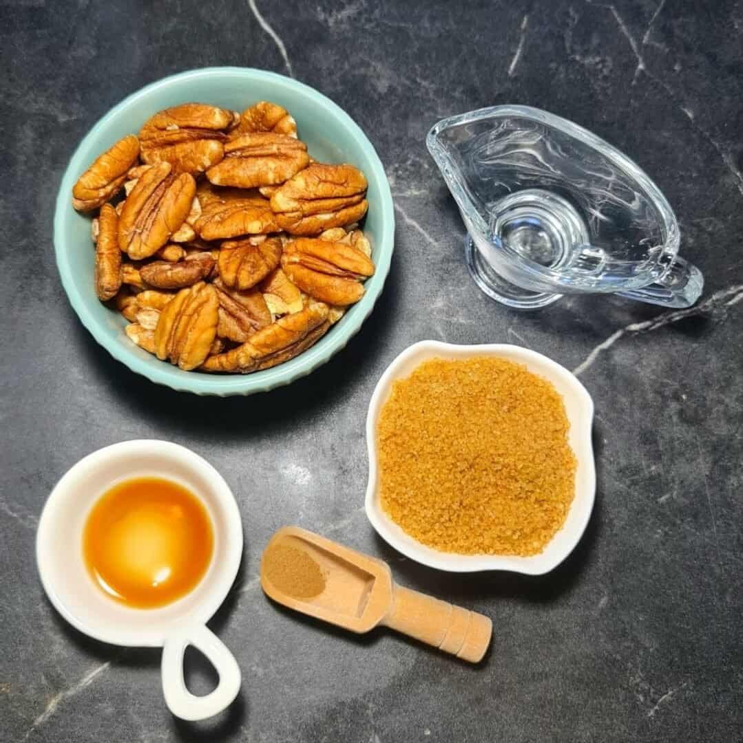  Ingredients for making candied pecans including pecans, brown sugar, vanilla extract, cinnamon, and water.