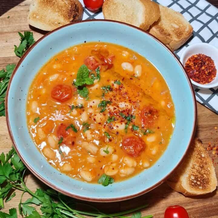 A bowl of hearty cannellini bean soup garnished with fresh herbs and served with toasted bread slices.