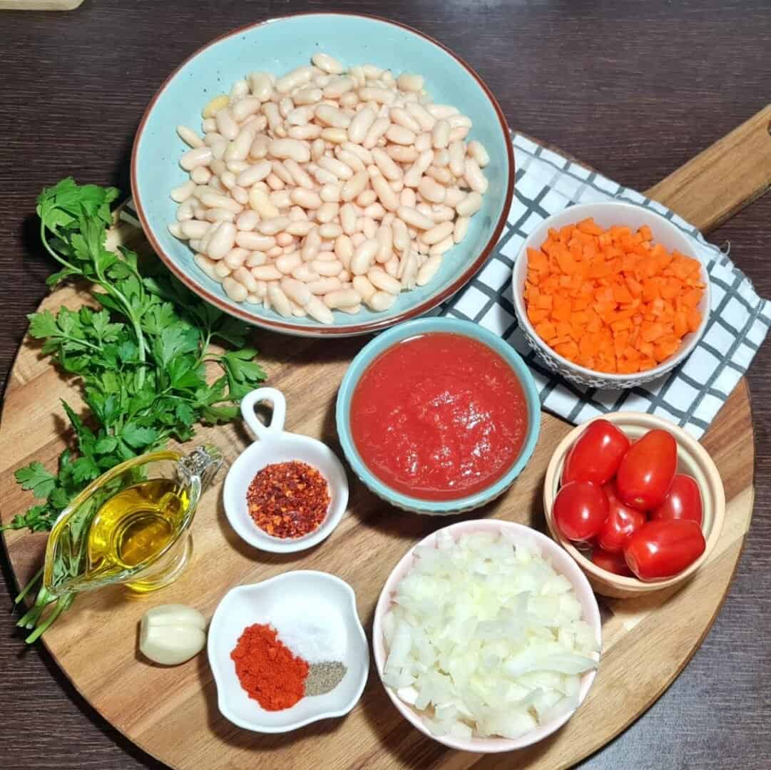  Ingredients for cannellini bean soup including cannellini beans, chopped carrots, tomato sauce, cherry tomatoes, chopped onions, parsley, olive oil, garlic, red pepper flakes, and spices.