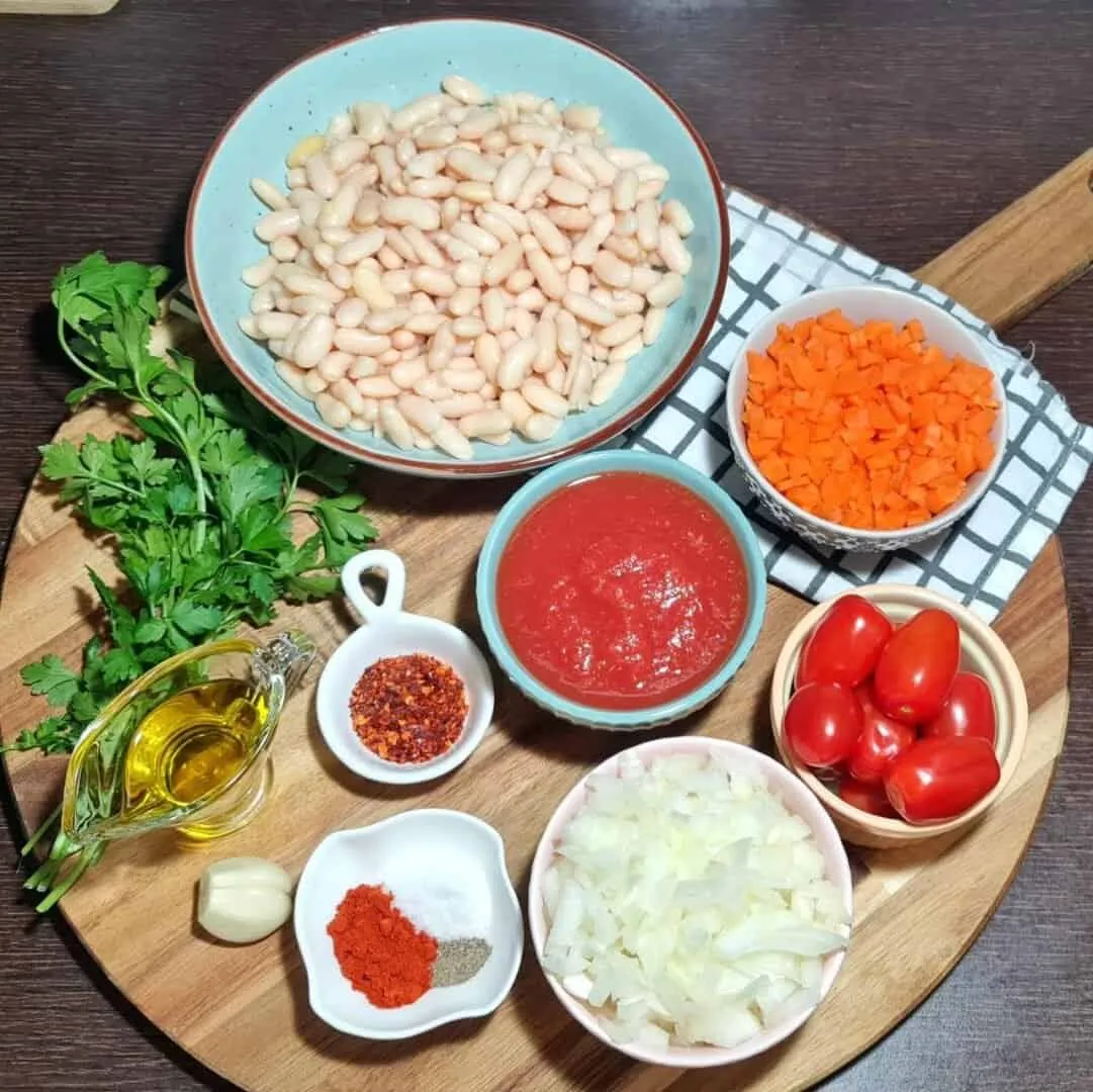  Ingredients for cannellini bean soup including cannellini beans, chopped carrots, tomato sauce, cherry tomatoes, chopped onions, parsley, olive oil, garlic, red pepper flakes, and spices.