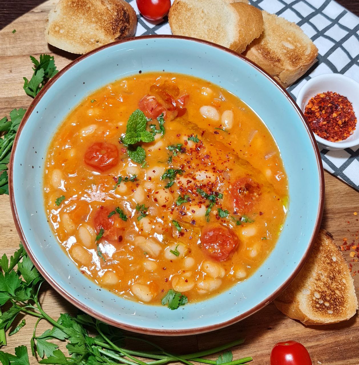 A bowl of hearty cannellini bean soup garnished with fresh herbs and served with toasted bread slices.