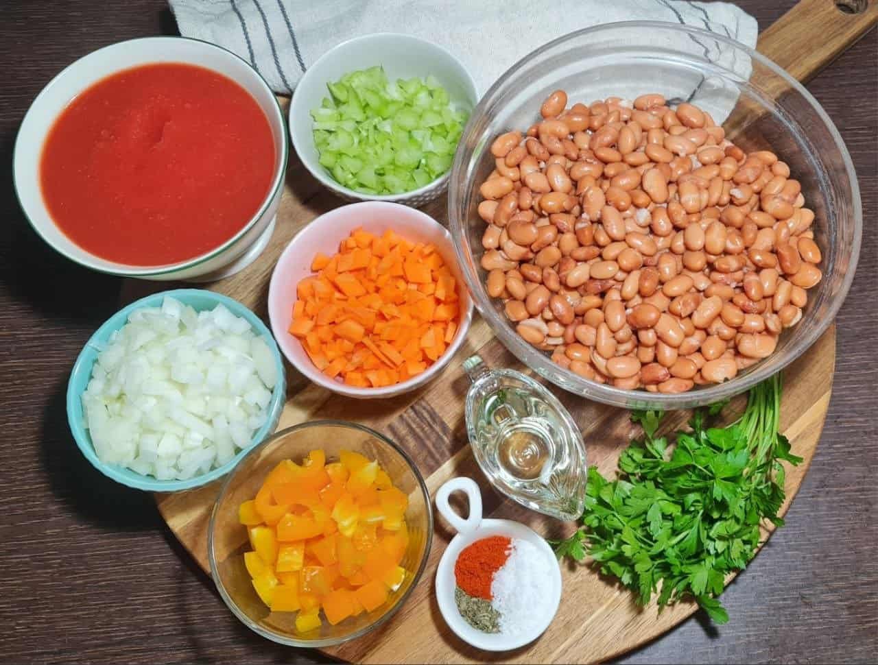  Ingredients for easy pinto bean soup, including pinto beans, diced vegetables, tomato puree, and spices, arranged on a wooden board.