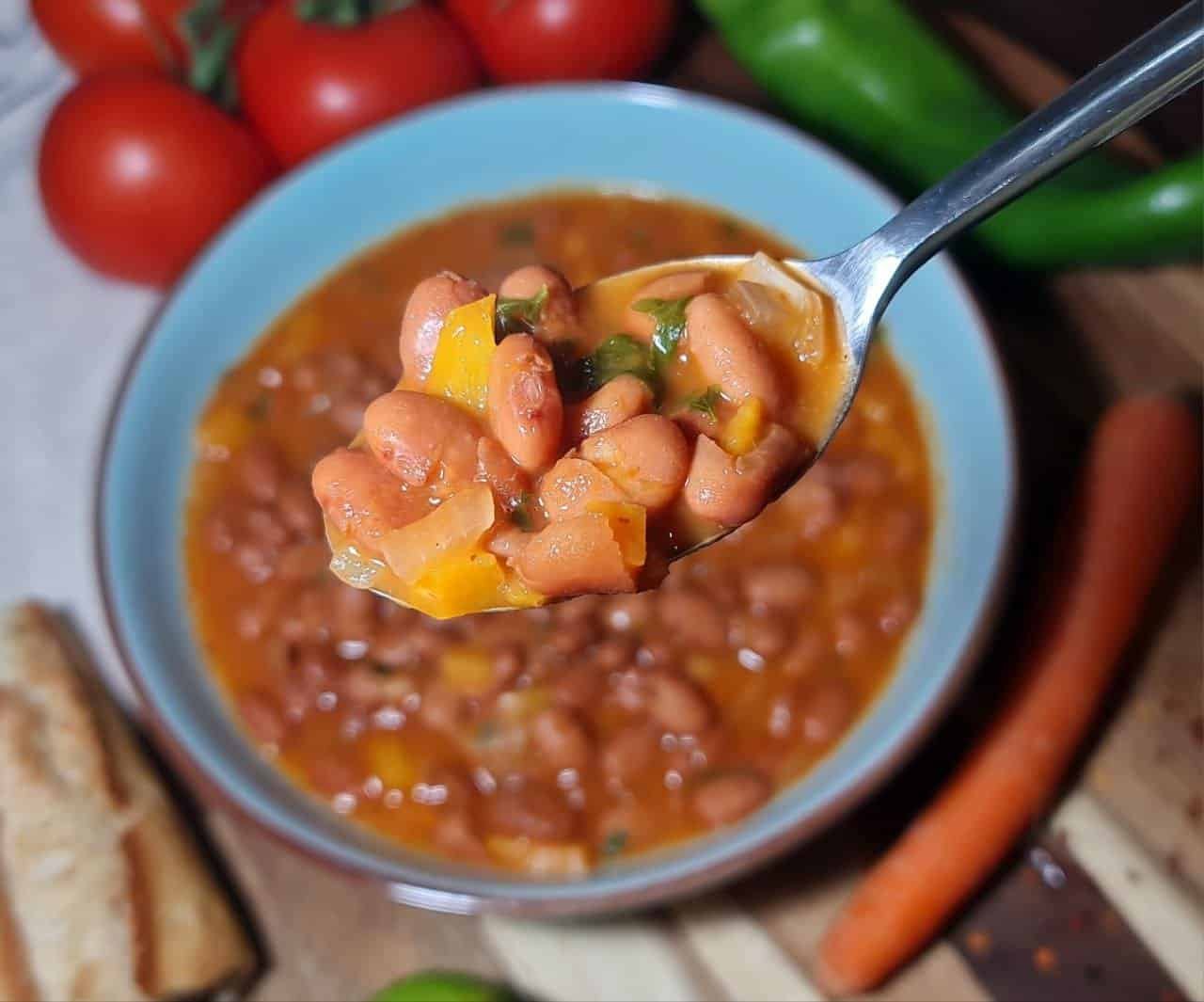 A spoonful of hearty pinto bean soup with diced vegetables, featuring a blue bowl in the background.