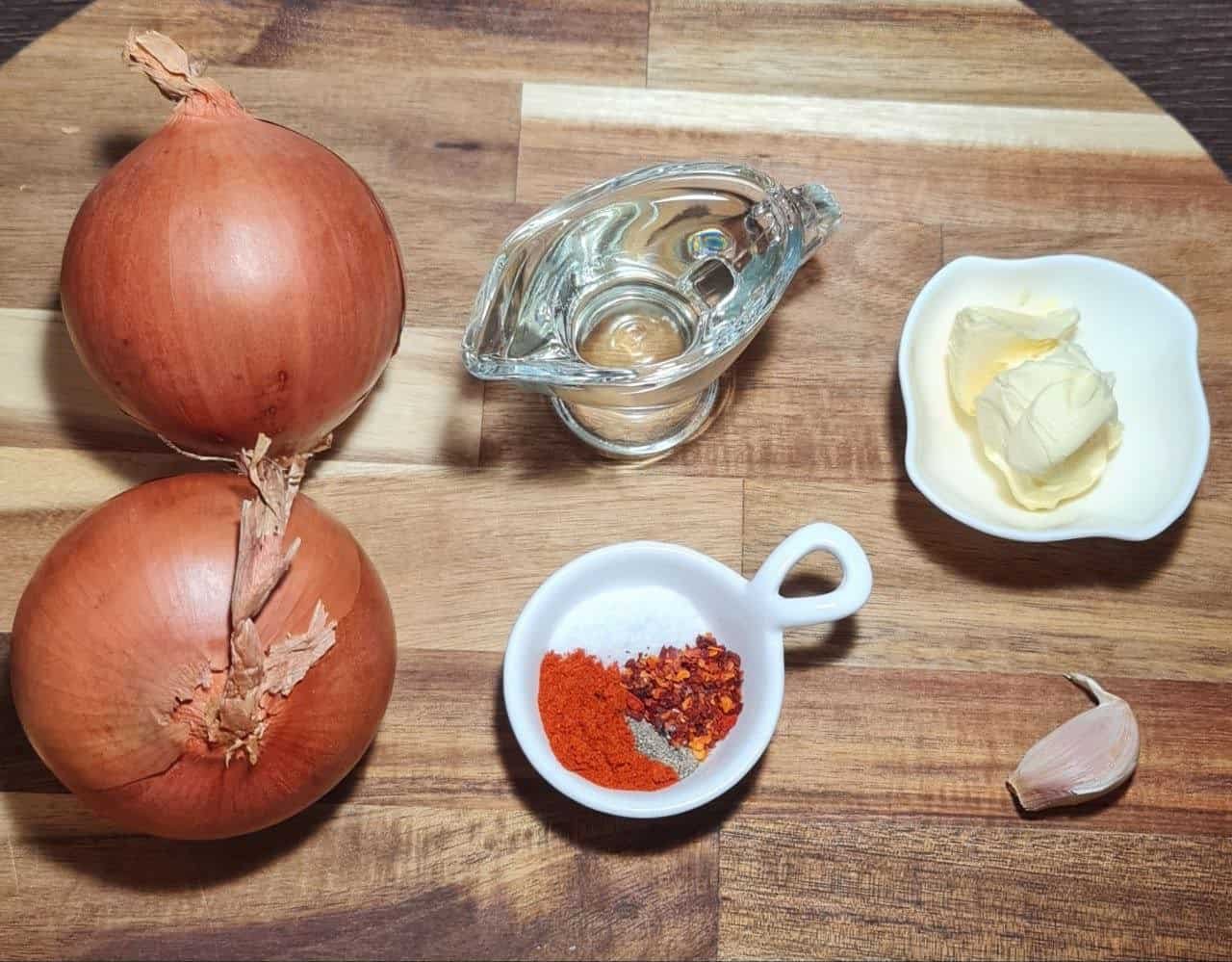 Two whole onions on a wooden surface with blurred background ingredients.